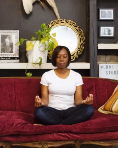 Woman sitting cross-legged on sofa with eyes closed in meditation 