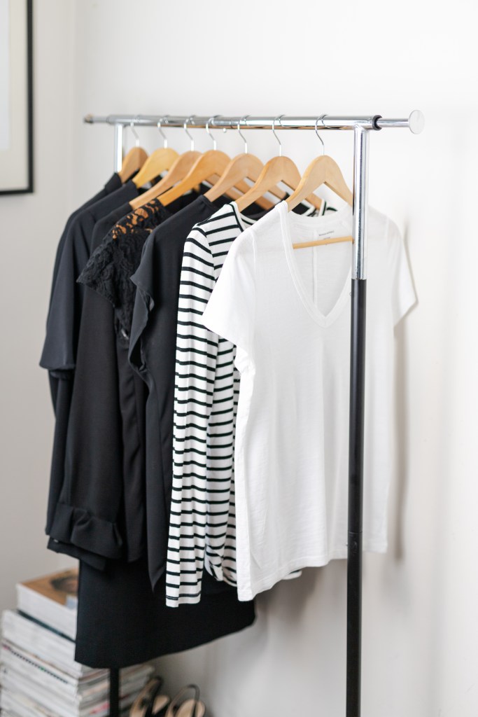 Metal rolling rack of black and white minimalist clothing hanging neatly on wooden hangers