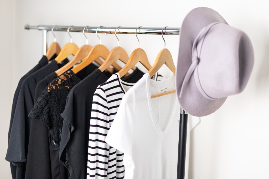Rolling rack of stylish, minimalist wardrobe pieces and a trendy pale purple broad-rimmed felt had
