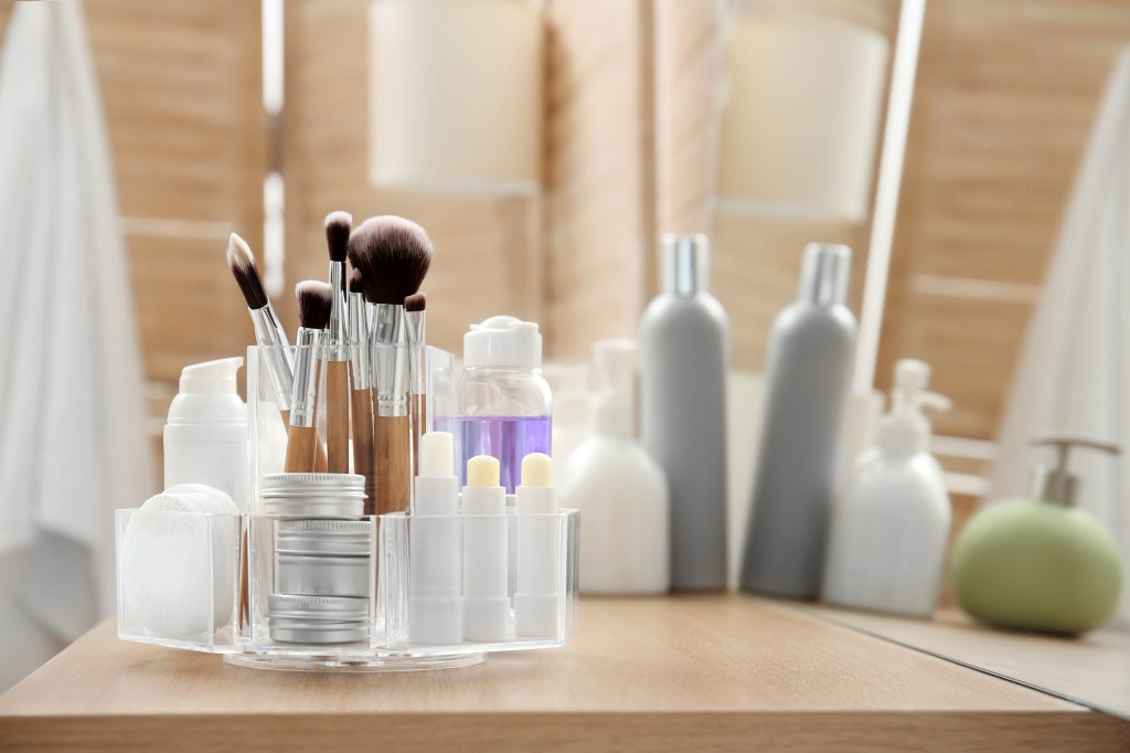 Makeup brushes and beauty products in clear organizer container on a bathroom counter