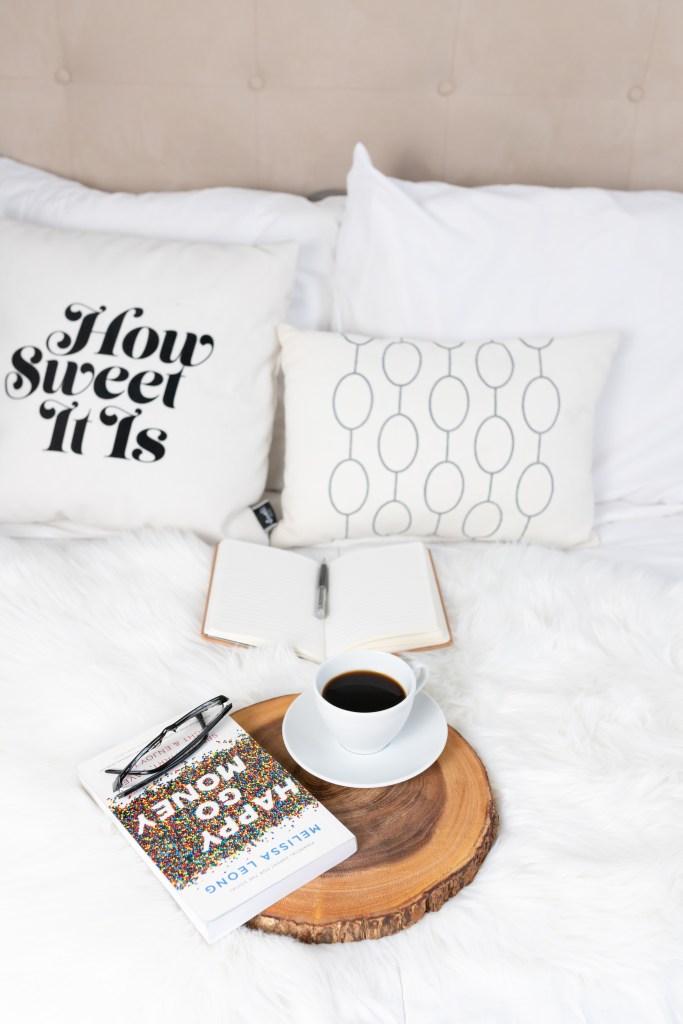 Photo of a Happy Go Money personal finance book on a breakfast tray with a cup of coffee on a bed. 